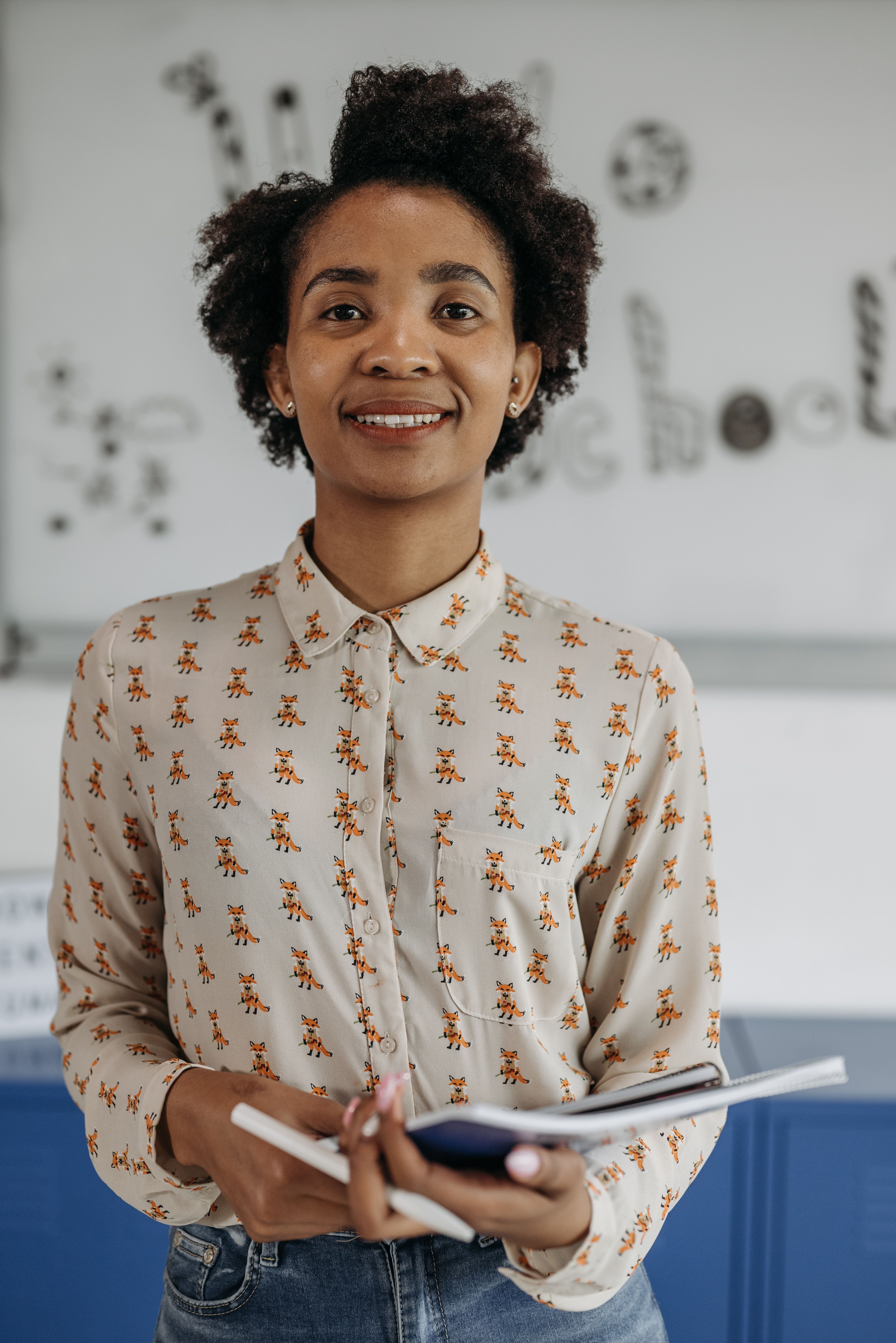 Female teacher smiling in a UK school classroom holding a folder